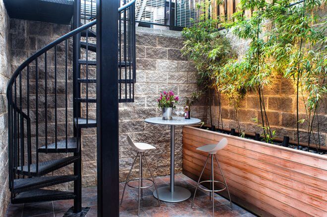 In an urban setting, any outdoor space is a luxury, even one below street level. You just have to make the most of it. A high-top table and tall planting bed complement the scale of this space. Leaves add softness and create a garden feel.