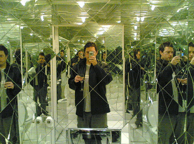 man taking a picture in a bathroom that is made of mirrors