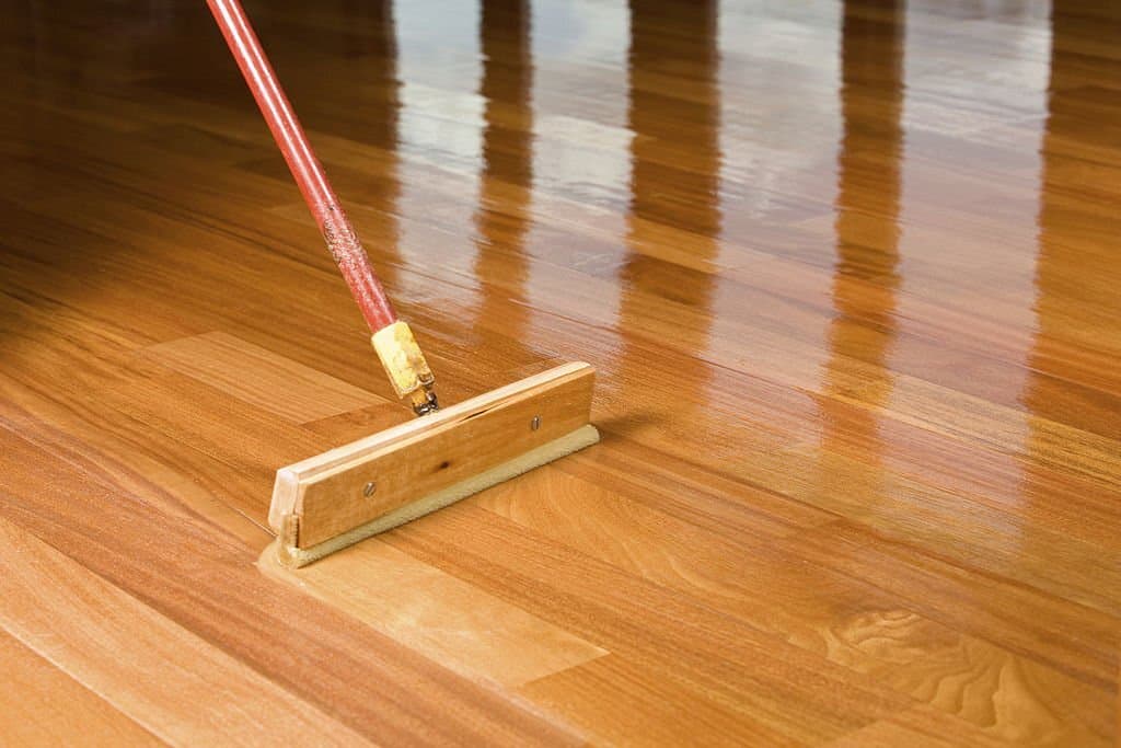 brush applying clear polyurethane to hardwood floor